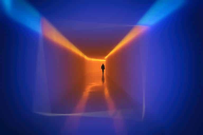Figure silhouetted in a brightly lit color tunnel installation