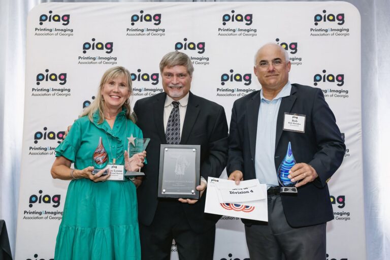 Three Drummond team members standing together at the PIAG imPRESS 2026 ceremony, holding the Best of Show star award, the Best of Division 4 certificate and two glass awards.